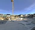 Large open area, construction site with foundation outlines, cranes present, neighboring houses visible
