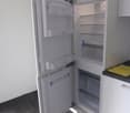 Open refrigerator, tile floor, kitchen cabinets, yellow paper on countertop, white walls