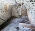 Small room with concrete floor, stone walls, and an arched passageway