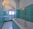 Bathroom with white tiles, turquoise tiles, bathtub, sink, radiator, window with curtains