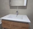 Bathroom with white sink, wooden drawers, and mirror with shower fixture