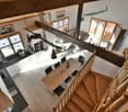 Open concept layout, wooden dining table, modern kitchen with granite countertop, modern staircase, wooden beams, cozy living area with sofa, glass windows, white walls