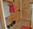 Wooden entryway with storage cabinets, coat hangers, and a red upholstered bench. Tile flooring and a rug in the entrance area.