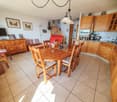 room features a wooden dining table and chairs, tiled floor, wooden cabinets, kitchen area with an oven, picture frames, staircase, television on a stand, and a lamp