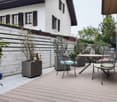 Table and chairs on deck with wooden railing, potted plants, and decorative items.