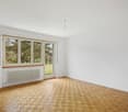Spacious room with large windows overlooking a garden, hardwood parquet flooring, and a radiator on the wall.