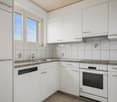 Fully equipped kitchen with granite countertops, integrated dishwasher, stainless steel sink, faucet, white cabinets, electrical outlets, and a window with outside view