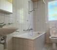 Tiled bathroom with a bathtub, sink, toilet, and a window