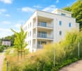 4 story building, balcony, metal fence, concrete walkway, lush vegetation, pink house in the background.