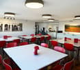 Dining tables, white chairs, pictures on wall, ceiling lamps, metal coat stand, white cabinets with countertops, coffee machine, microwave, refrigerator
