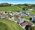 Complex of buildings in an urban area, multiple parking spaces, grassy fields, and trees.