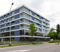 6-storey blue building, windows with black frames, outdoor plants, empty parking space