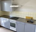 Stainless steel counter, kitchen cabinets, electric stove, oven, sink, tiled walls, power outlet, exhaust hood