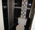 a shower enclosure, a white toilet bowl, tiled walls and floor, a towel hanging on a rack