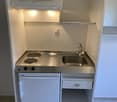 Kitchen: gas stove, stainless steel sink, cabinet, small refrigerator, under-mounted sink, overhead cabinet, white walls, tiled floor.