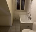 bathroom with bathtub, toilet, and sink. Tiled floor and walls, small window with reflection.