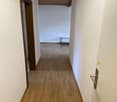 Empty hallway with wooden floor and white walls, wooden ceiling, two doors on the left, a small table in the distance