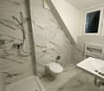 Bathroom with marble-like tile walls, shower stall, toilet, and vanity