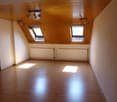 Spacious attic room with wooden ceiling and walls, two large windows, and hardwood flooring. The room appears to be empty and ready for furnishing.
