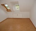 Spacious attic bedroom with wooden parquet flooring, white walls, and a skylight window providing natural light. The room appears to be empty and ready for furnishing.