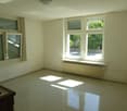 Empty room with white walls, large windows, and tile flooring. The room appears to be a living room or bedroom with no furniture or decor visible.