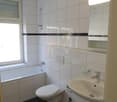 Bathroom with white tiles, toilet, sink, and window