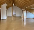 Large open attic space with wooden beamed ceiling, white walls, and hardwood flooring. The space appears to be unfinished and could potentially be converted into additional living space.