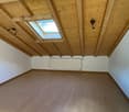 Spacious attic room with wooden beamed ceiling, skylights, and hardwood flooring. The room appears to be empty and ready for furnishing.