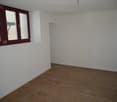 Empty room with white walls, hardwood floor, and large windows with burgundy frames.