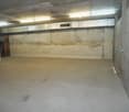 Large open basement space with concrete walls and floor, fluorescent lighting, and a ventilation system visible.