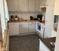 Fully equipped kitchen with white cabinets, wooden countertops, tile flooring, dishwasher, and washing machine