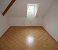 Spacious attic bedroom with slanted ceiling, hardwood parquet flooring, and a window providing natural light.