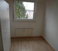 empty room with a door, window, white radiator, wooden floor, and white walls