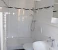 Bathroom with a toilet, a shower, and a sink. The walls are tiled in white with black stripes, and the floor is black tile. A mirror is mounted on the wall above the sink.