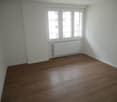 Empty room with white walls, wooden floor, white radiators, window.