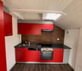 red cabinets, wooden floor, gray countertop, modern appliances, ceiling light