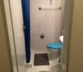 Bathroom with blue shower curtain, white tiled floor, white toilet, white sink, rug and toilet paper