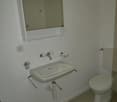 bathroom with toilet, sink, toilet paper holder, mirror with illuminated light, wall mounted electrical outlet
