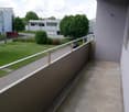 concrete balcony with metal railings, grass field, road, buildings, tree, car