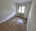 Empty room with wooden floor and white walls, large window with blinds, radiator