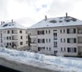 Multi-story apartment building with white exterior, snow-covered roofs, and balconies visible.