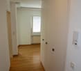 empty hallway, wooden floor, white walls, built-in wardrobes, small window with blinds, power outlet, no furniture