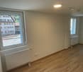 Empty room with wooden floors, white walls, two windows, and white radiators