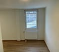 Empty room with white walls, wooden floors, single window, and radiator.