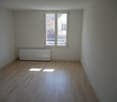 Empty room with white walls, wooden floor, window, and a radiator.