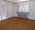 Empty room with white walls, wooden tile floor, sliding glass doors, two windows with white blinds, and a radiator.