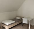 small room, bed with pillows, desk, white chair