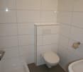 Small bathroom with white walls, floor and ceiling, white sink, white toilet, shower