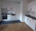 Spacious kitchen with white cabinets, black countertops, gas stove, and dishwasher. Hardwood flooring and tiled floor in the kitchen area.