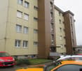 multi-storey residential building, beige and brown facade, several windows, balcony, parked cars